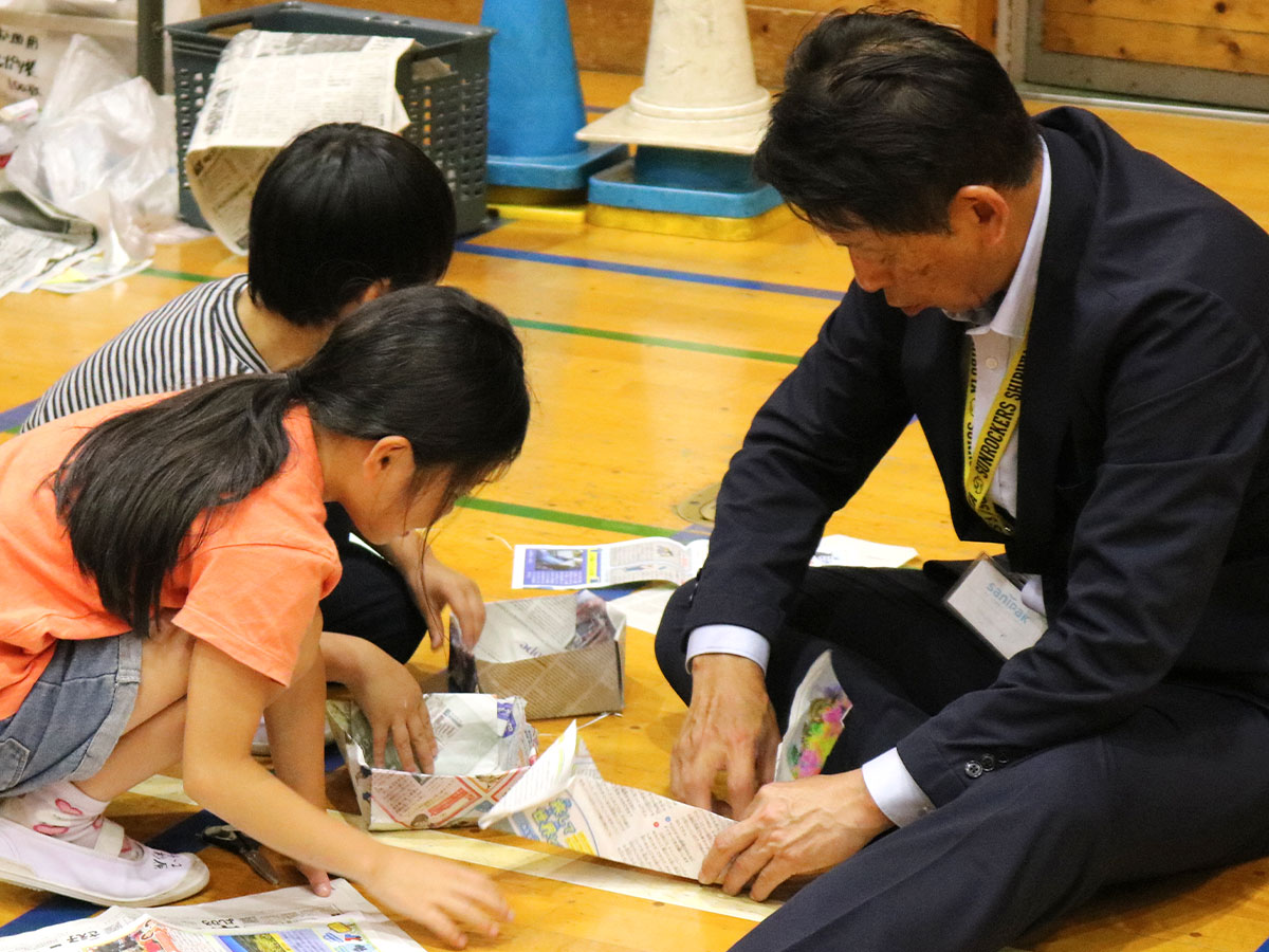 こどもたちと一緒に、新聞紙でお皿の土台を作る代表井上